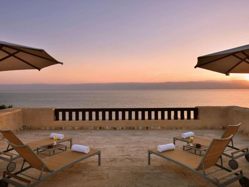 Quatre chaises longues vides sur une terrasse en pierre dominant la mer lors d'un coucher de soleil coloré.