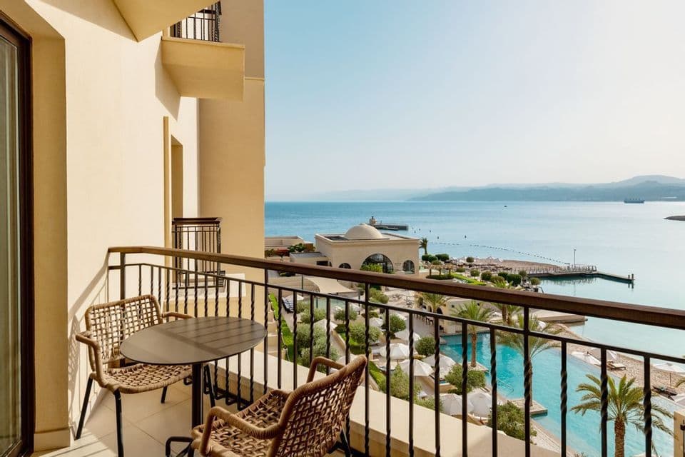 Una vista desde el balcón de un hotel con mesa y sillas, con vistas a una piscina, la playa y el mar.