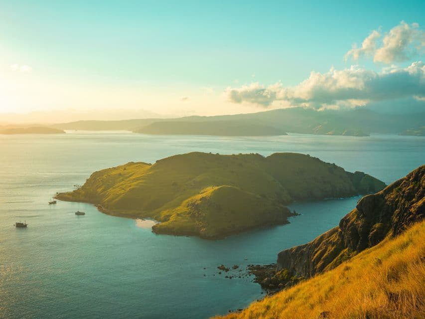Una vista aerea di isole verdi e ondulate e alcune barche in acque calme e turchesi durante un tramonto dorato.