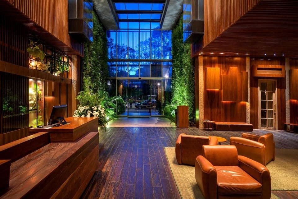 El vestíbulo de un hotel moderno con paneles de madera, jardines verticales iluminados y una zona de asientos con sillones de cuero.