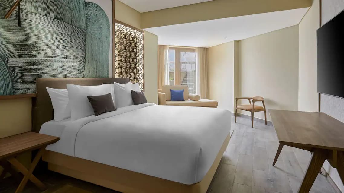 Une chambre d'hôtel avec un lit king-size impeccablement fait, une grande tête de lit abstraite verte, un bureau en bois et une chaise longue.