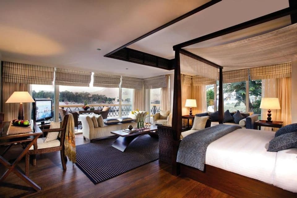 Une suite d'hôtel avec un lit à baldaquin, un coin salon et de grandes fenêtres donnant sur un balcon et une rivière.