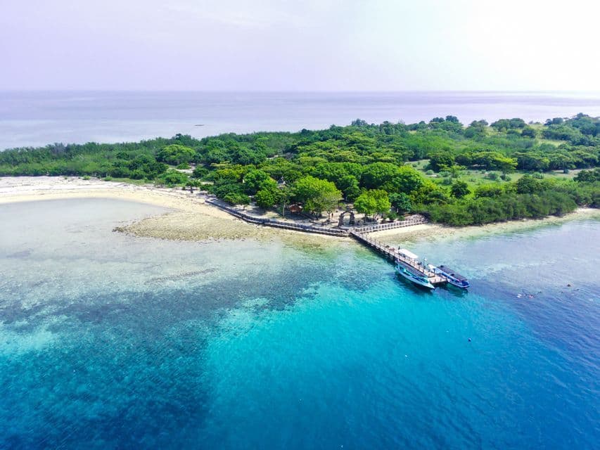 Vista aerea di una piccola isola tropicale con un molo di legno dove due barche sono ormeggiate in acqua turchese.