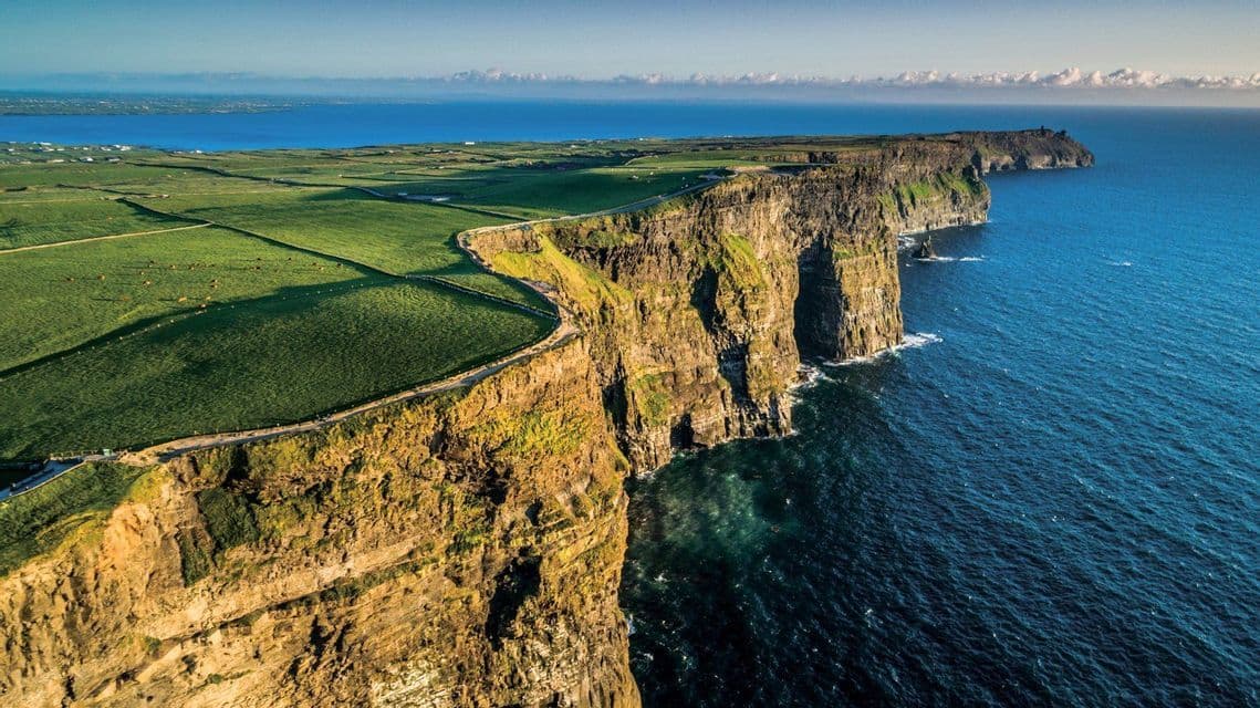 Vista aerea di scogliere a picco, coperte di verde, che si gettano in un oceano blu profondo, con un sentiero che costeggia il bordo.