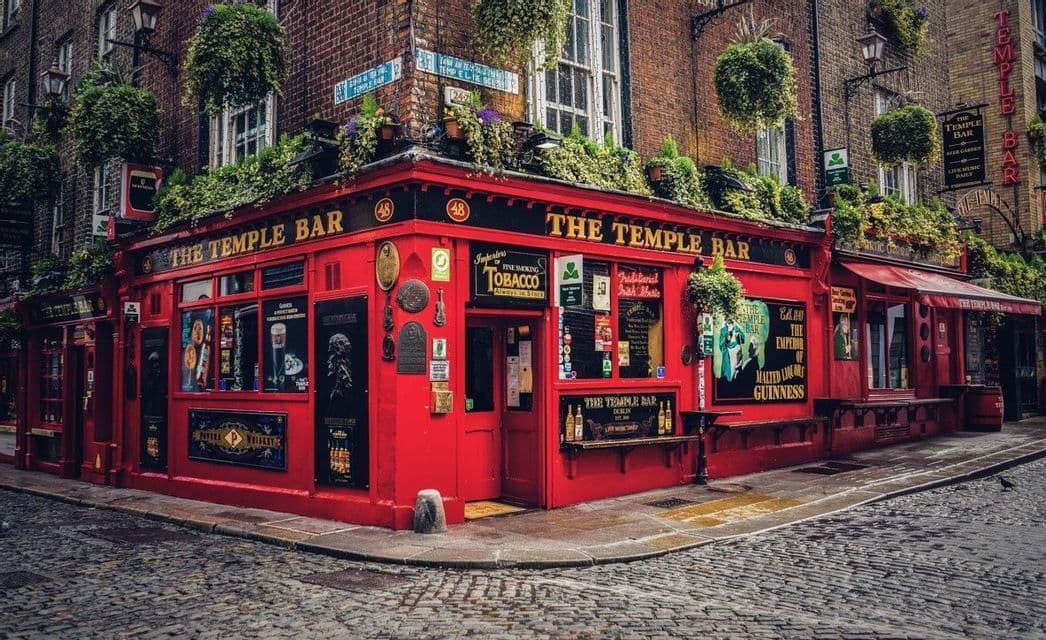 La facciata rosso vivo del pub The Temple Bar su un angolo di strada acciottolata, decorata con piante verdi pendenti.