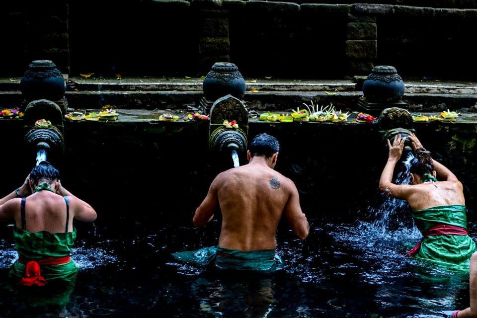 Un viaje en grupo de WeRoad, visto desde atrás, participando en un ritual de purificación bajo fuentes de agua de piedra en una poza oscura.