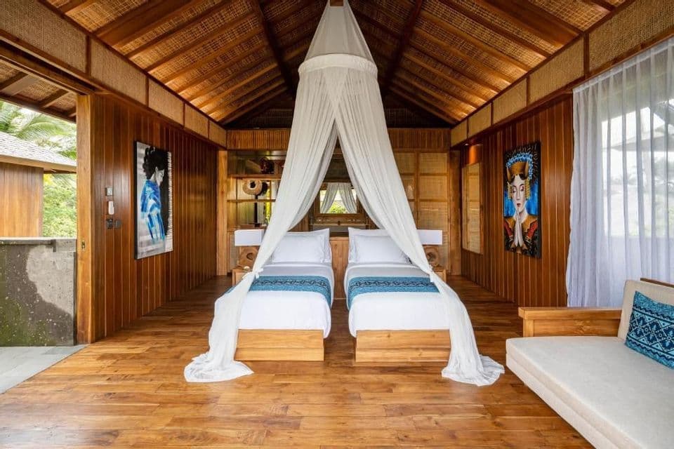 Intérieur d'une spacieuse chambre lambrissée de bois, avec deux lits simples sous une moustiquaire blanche à baldaquin.