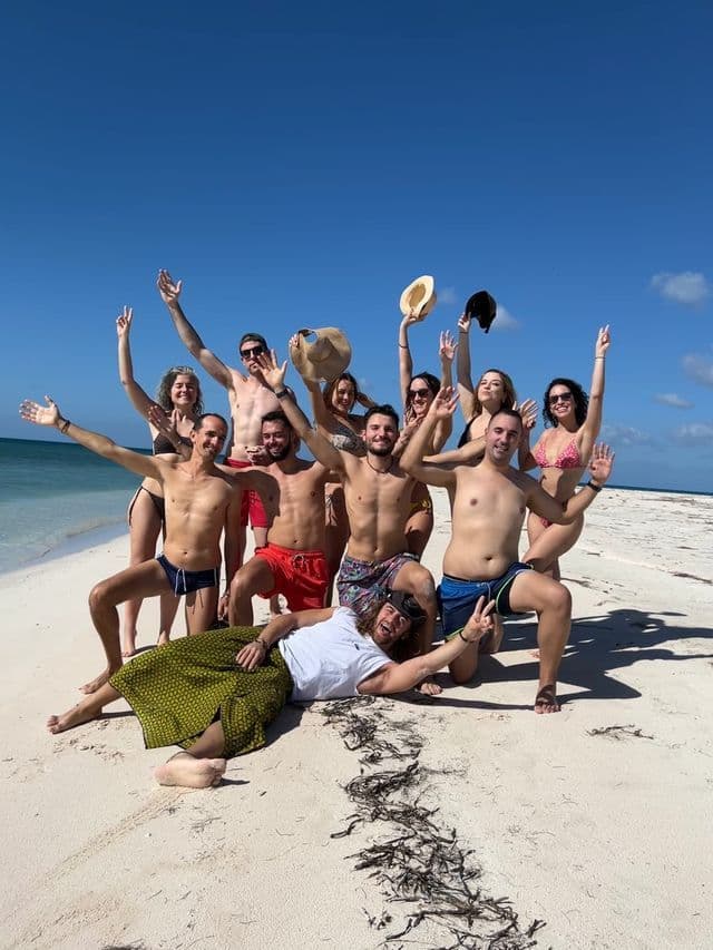 Un groupe WeRoad souriant et posant pour une photo sur une plage de sable blanc sous un ciel dégagé.