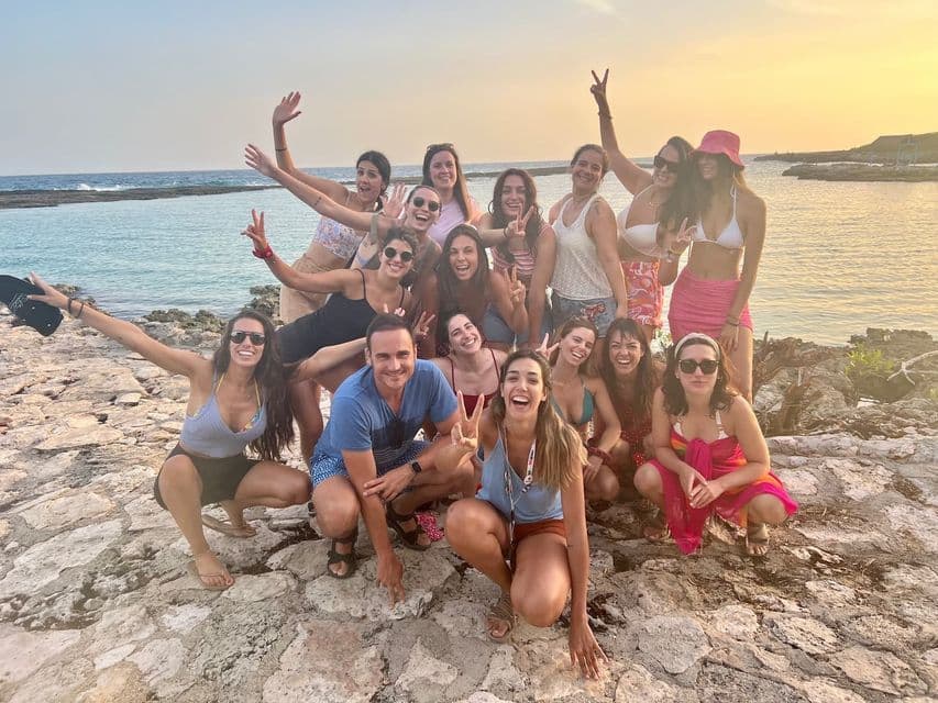 Eine WeRoad-Gruppe lächelt und posiert bei Sonnenuntergang für ein Foto an einem felsigen Ufer am Meer.