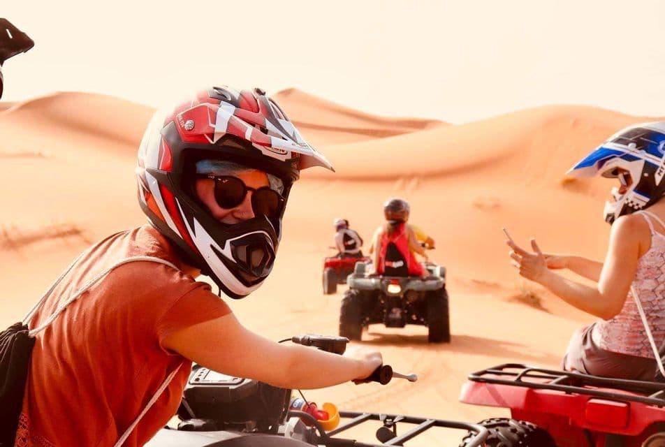 Un voyage de groupe WeRoad en quad, casqués, à travers de grandes dunes de sable du désert.