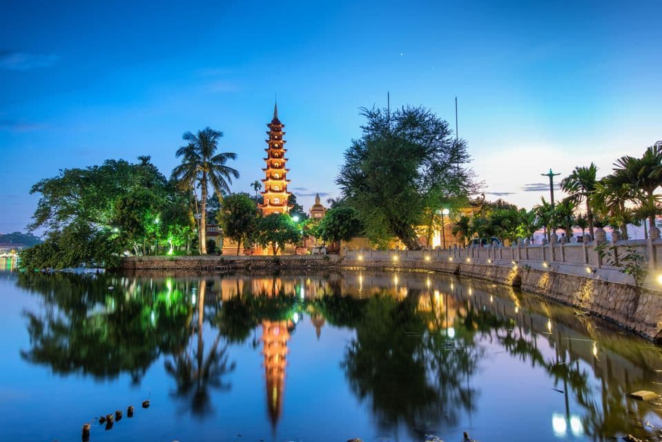 Une tour de pagode illuminée et les arbres environnants se reflétant dans l'eau calme au crépuscule.