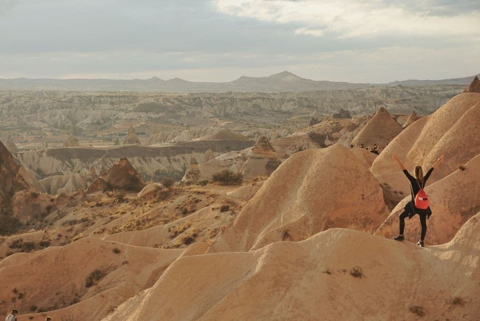 Una persona en un viaje en grupo de WeRoad está de pie con los brazos en alto, contemplando un vasto valle con formaciones rocosas distintivas.