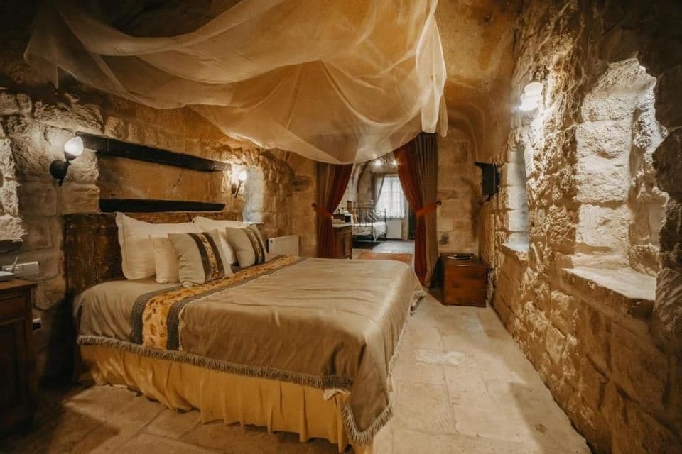 Una habitación rústica dentro de una estancia tipo cueva con paredes de piedra vista, que cuenta con una cama grande con dosel transparente.