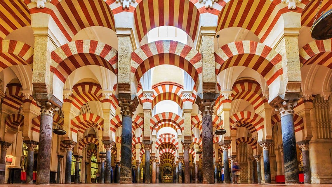 The interior of a large hall filled with columns supporting distinctive red and white striped arches.