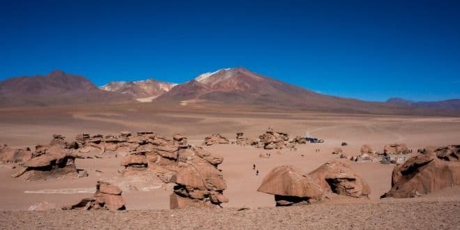 Un viaje en grupo WeRoad explora formaciones rocosas únicas en un vasto desierto con montañas distantes bajo un cielo azul claro.