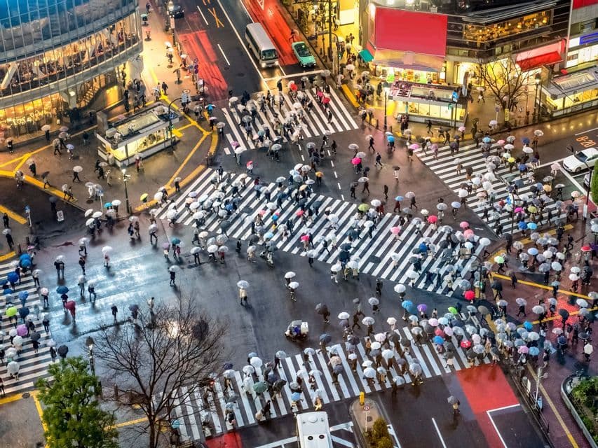 Vue aérienne de piétons avec des parapluies traversant un carrefour urbain animé un jour de pluie.