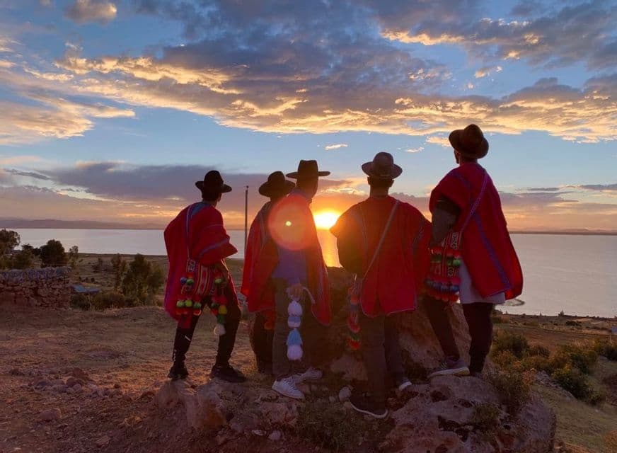 Eine WeRoad-Gruppe mit roten Ponchos und Hüten beobachtet den Sonnenuntergang von einem Hügel mit Blick auf einen großen See.