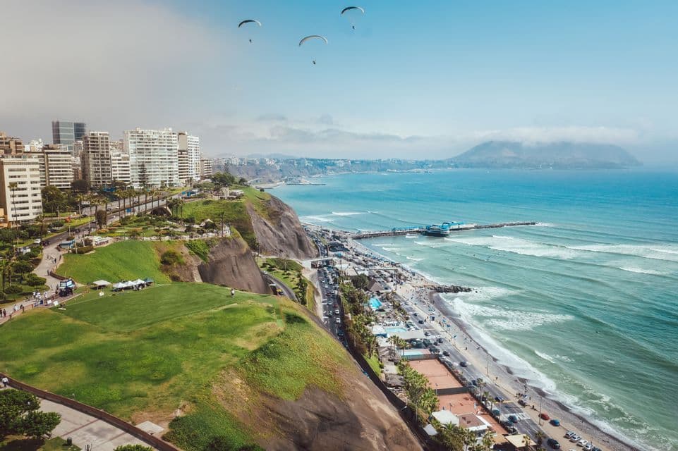 Eine Luftaufnahme einer Küstenstadt auf Klippen, mit mehreren Paraglidern, die über dem Meer fliegen, und einem Pier.