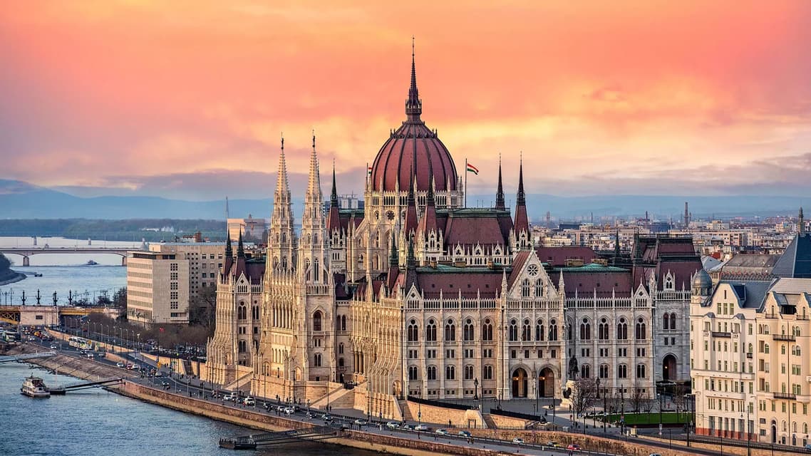 The spires of the Hungarian Parliament in Budapest against a pink sunset sky.