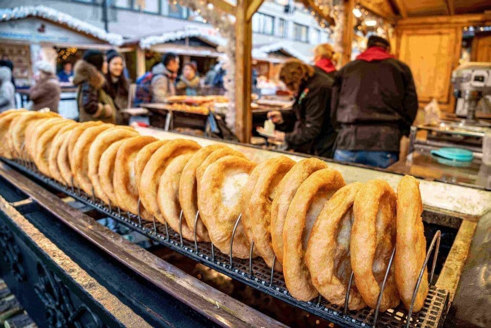 Una larga hilera de aros de masa frita dorados en un puesto de comida en un mercado al aire libre.