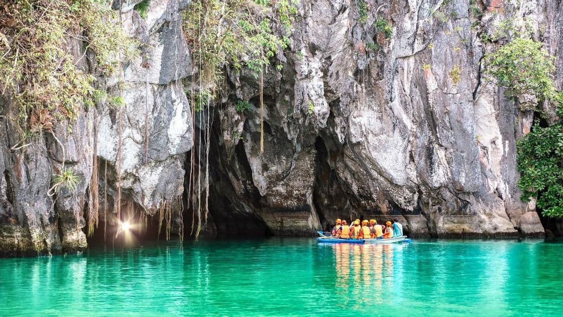 Un viaggio di gruppo WeRoad in barca si avvicina a una grande grotta marina con acqua turchese e una luce che filtra dall'ingresso.