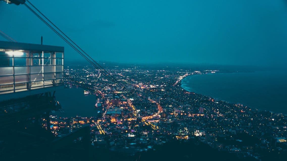 Vista panoramica da una stazione della funivia che si affaccia su una città costiera illuminata al tramonto.