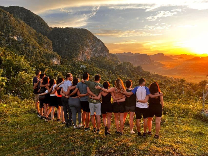 Eine WeRoad-Reisegruppe steht Arm in Arm auf einem Hügel und beobachtet den Sonnenuntergang über einem üppigen Bergtal.