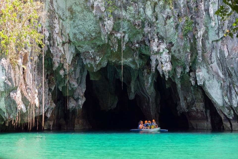 A WeRoad group trip in a small boat at the entrance of a large sea cave with turquoise water.