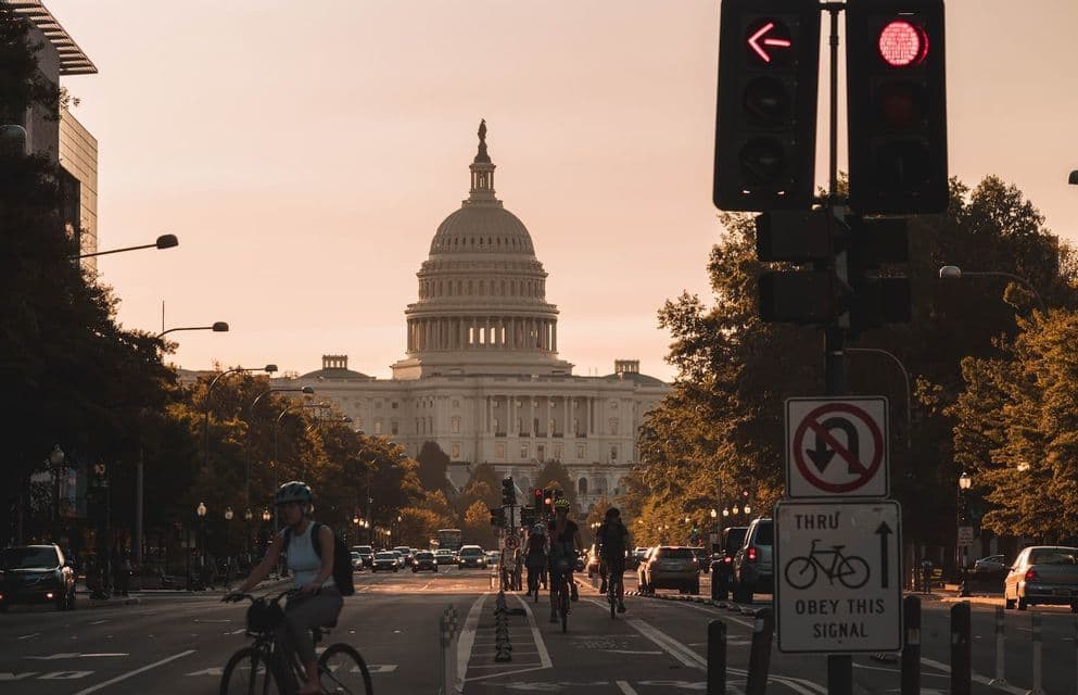 Ciclistas bajan por una calle de la ciudad con el Capitolio de EE. UU. al fondo durante un atardecer dorado.