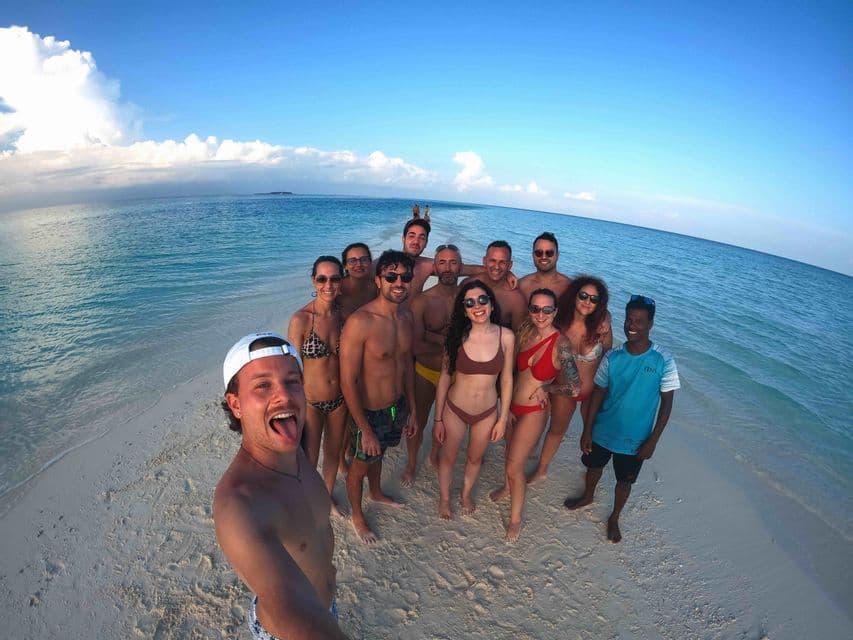Un gruppo WeRoad scatta un selfie di gruppo su una stretta lingua di sabbia, circondato da acque oceaniche calme e turchesi.