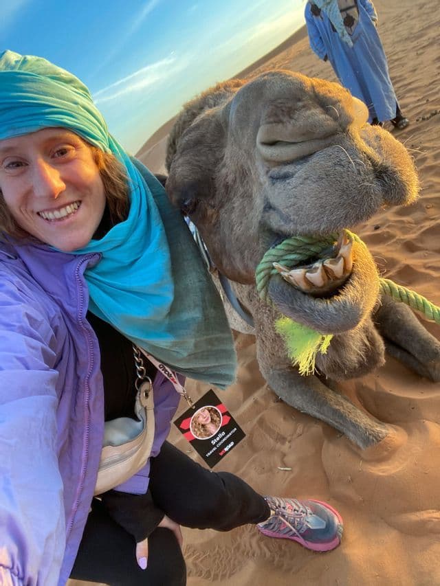 Una donna in viaggio di gruppo WeRoad scatta un selfie sorridente con un cammello nel deserto.