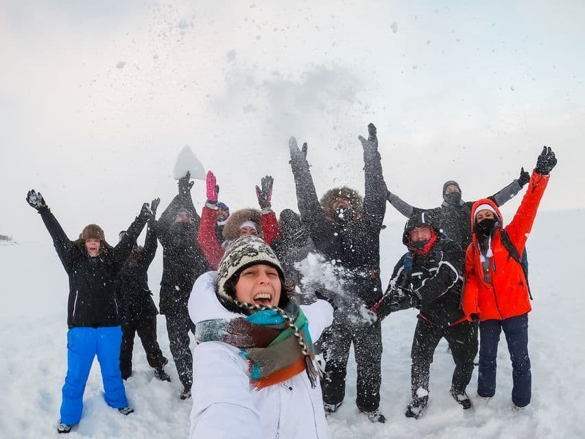 Una mujer se hace una selfie con su grupo de WeRoad mientras animan y lanzan nieve en un extenso paisaje nevado.
