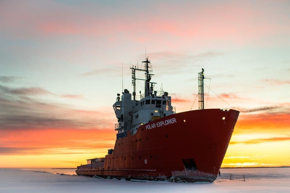Le brise-glace rouge Polar Explorer est posé sur une vaste étendue de mer gelée sous un ciel de coucher de soleil coloré.