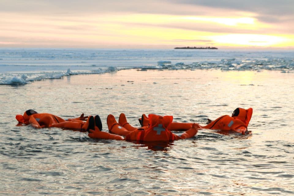 Un voyage de groupe WeRoad en combinaisons d'immersion oranges flottant sur le dos dans l'eau glacée au coucher du soleil.