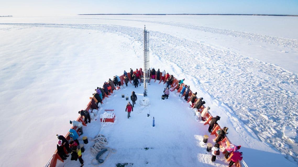 Un groupe WeRoad en voyage debout sur la proue enneigée d'un brise-glace, naviguant à travers une vaste mer gelée.