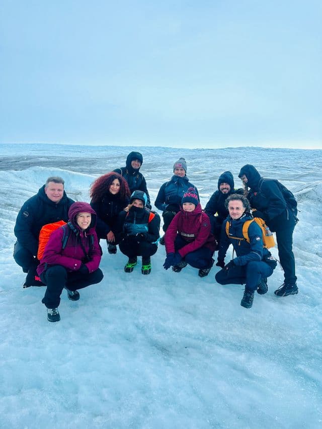 Un viaggio di gruppo WeRoad con abbigliamento invernale, in posa per una foto su un grande ghiacciaio sotto un cielo coperto.