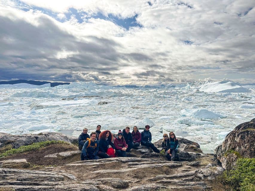 Un gruppo WeRoad in posa su una sporgenza rocciosa che domina un mare ricco di iceberg e ghiacciai sotto un cielo nuvoloso.