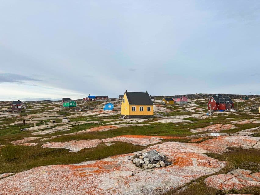 Un villaggio di case di legno colorate sorge su un paesaggio roccioso e coperto di licheni sotto un cielo nuvoloso.