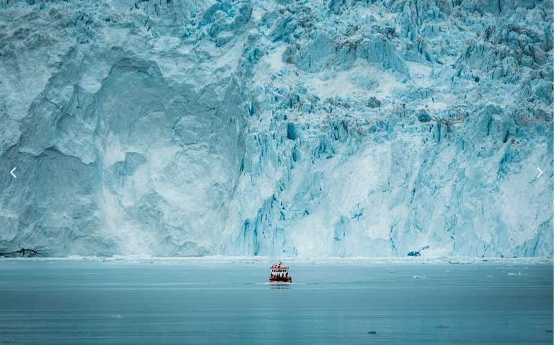 Una barca turistica rossa e bianca, con a bordo un gruppo WeRoad, naviga su acque calme di fronte a un'imponente parete di ghiacciaio blu.
