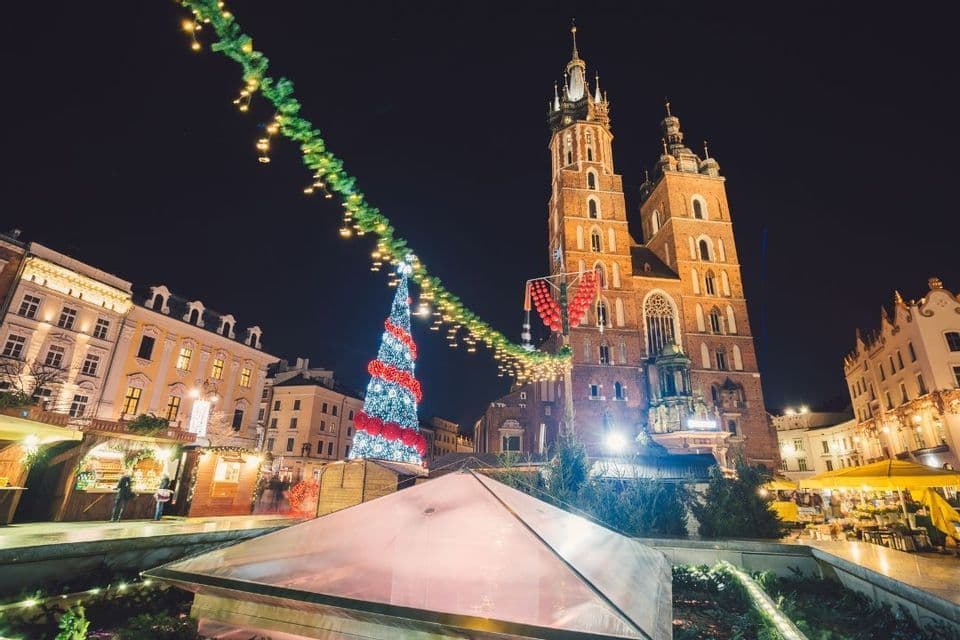 Un mercatino di Natale in una piazza cittadina di notte, con un albero illuminato e una storica cattedrale in mattoni sullo sfondo.
