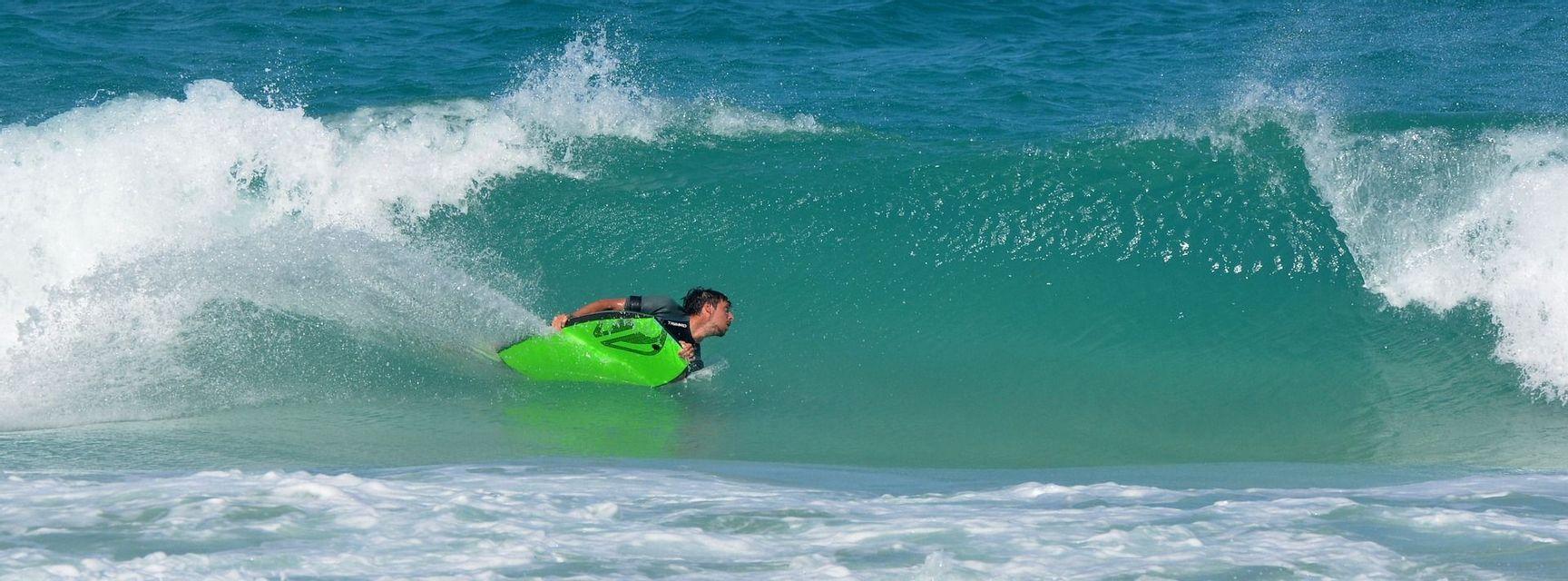 Un uomo su un bodyboard verde brillante cavalca all'interno del tubo di un'onda turchese che si infrange.
