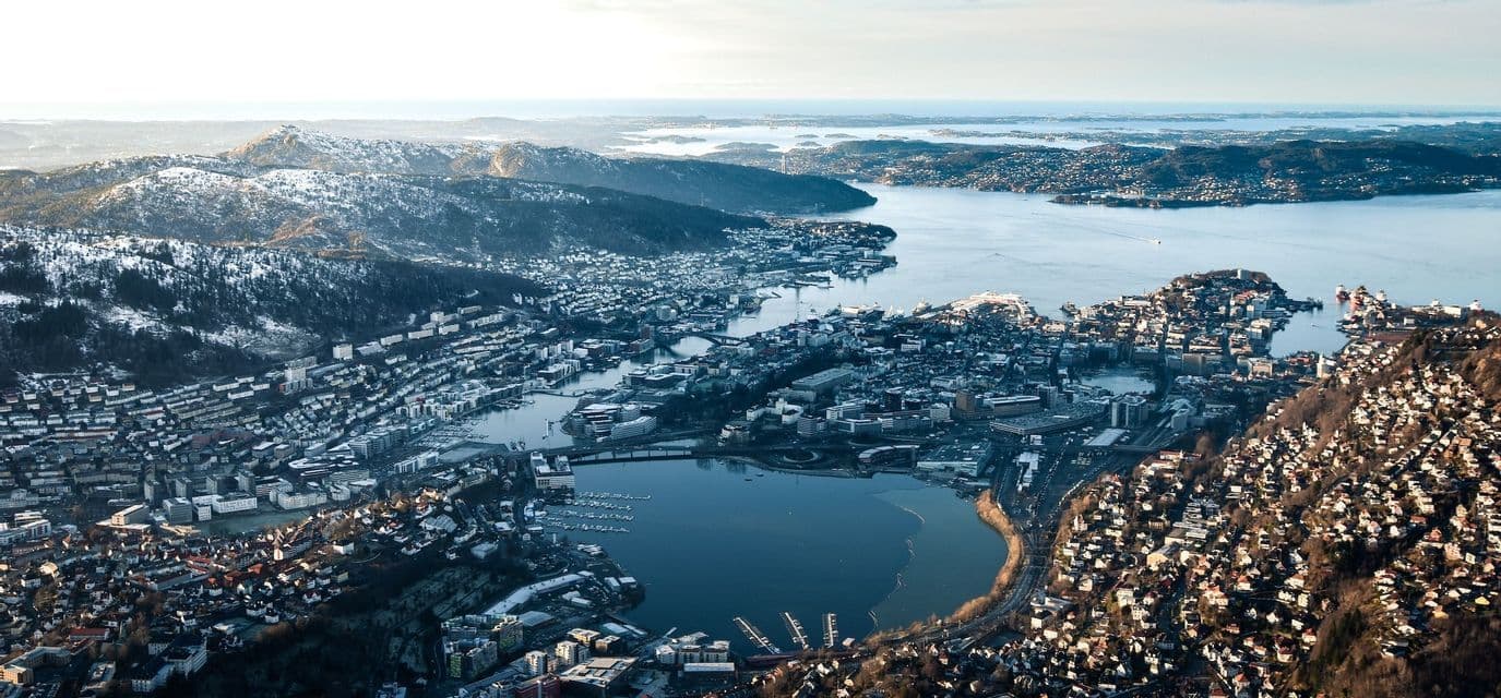 Una vista aerea di una città costiera situata tra montagne innevate e un grande specchio d'acqua con isole.
