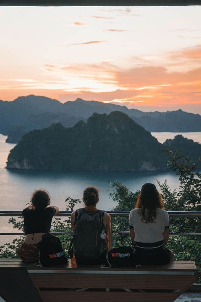 Viaggio di gruppo WeRoad: tre persone su una panchina con vista baia e isole al tramonto.