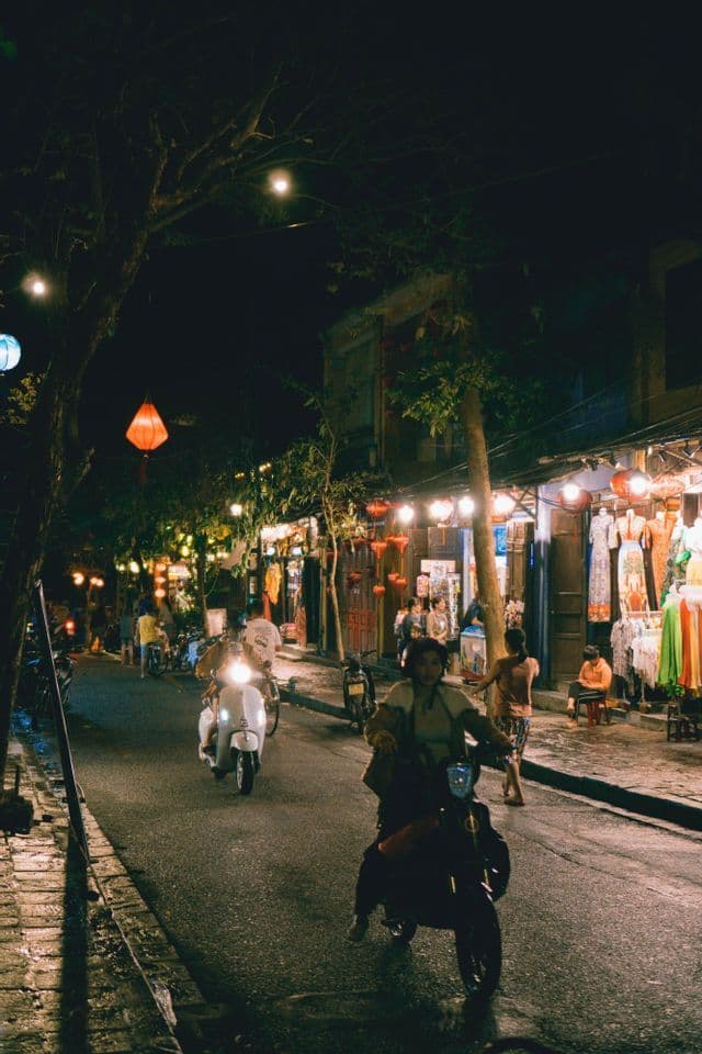 Una vivace scena di strada notturna con persone in scooter, negozi illuminati e lanterne di carta luminose