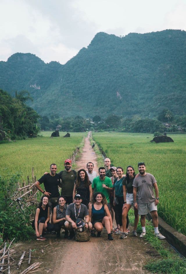 Un gruppo WeRoad in posa per una foto su un sentiero sterrato tra risaie, con lussureggianti montagne verdi sullo sfondo.