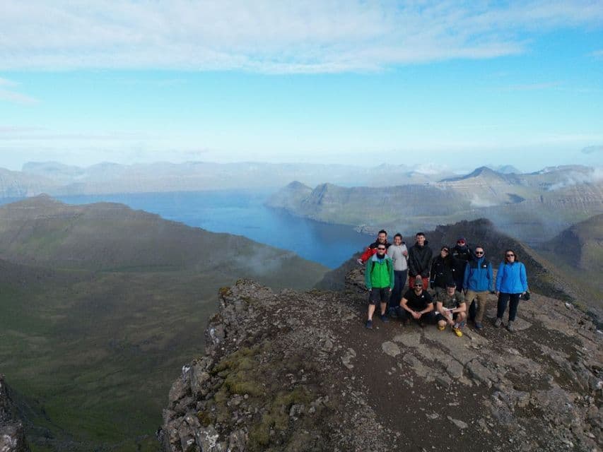 Un gruppo WeRoad in viaggio posa per una foto su una cima rocciosa, con vista panoramica su fiordi e colline sullo sfondo.