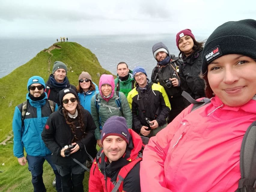 Un gruppo WeRoad si scatta un selfie su una scogliera erbosa a picco sul mare, tutti con giacche calde e berretti.