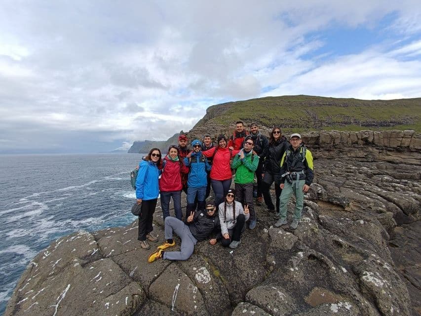 Un viaggio di gruppo WeRoad in posa per una foto su una scogliera rocciosa a picco sul mare sotto un cielo nuvoloso.