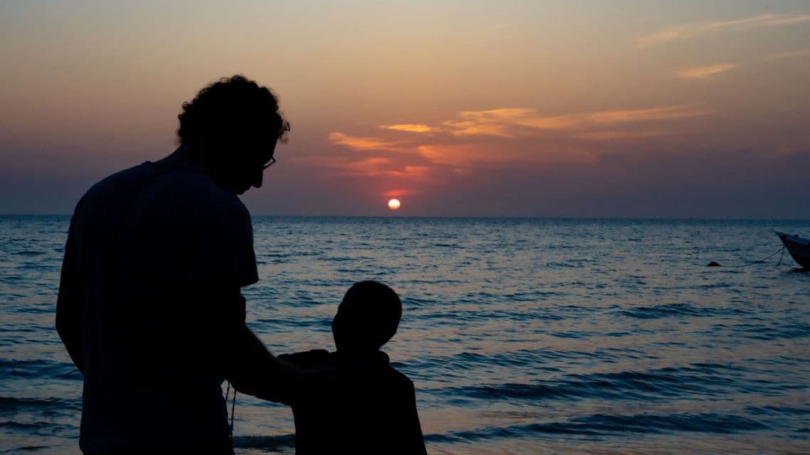 Sagome di un adulto e un bambino in piedi su una spiaggia mentre osservano il tramonto sull'oceano.
