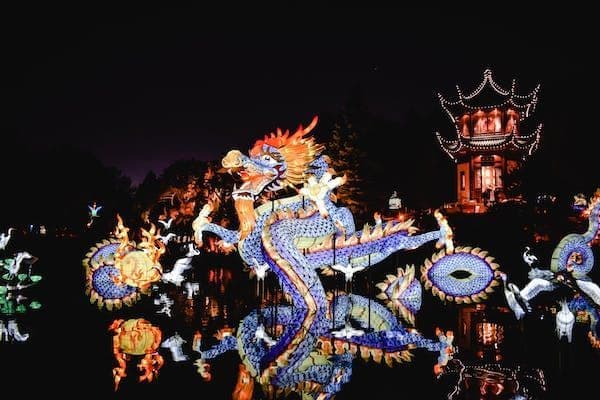 Una lanterna a forma di drago cinese illuminata galleggia sull'acqua di notte, con una pagoda illuminata sullo sfondo che si riflette sulla superficie.